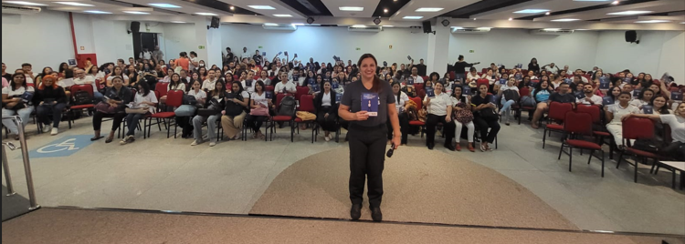 Imagem de palestra lotada com público feminino em grande auditório